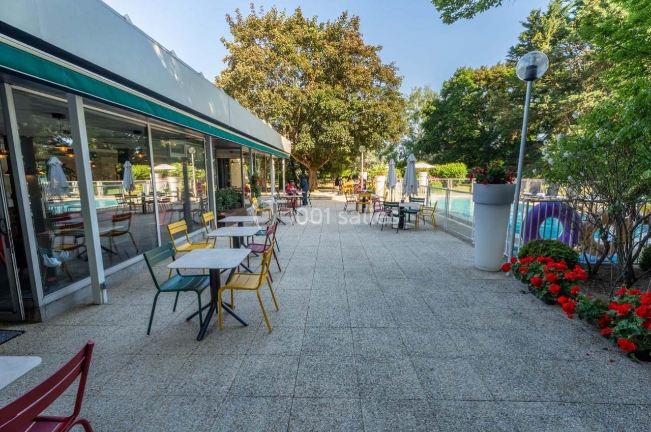 Terrasse extérieure avec tables et chaises colorées, bordée de fleurs et d'arbres, près d'une piscine.