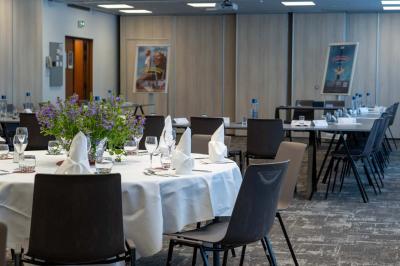 Chambre avec un lit double, un canapé gris, un mur clair et un tableau encadré.