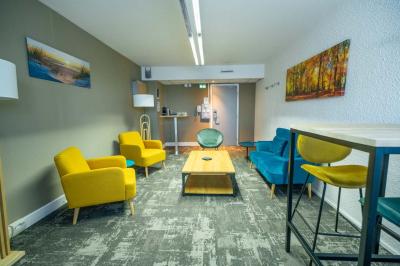 Chambre avec un lit double, un canapé gris, un mur clair et un tableau encadré.