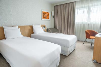 Chambre avec un lit double, un canapé gris, un mur clair et un tableau encadré.