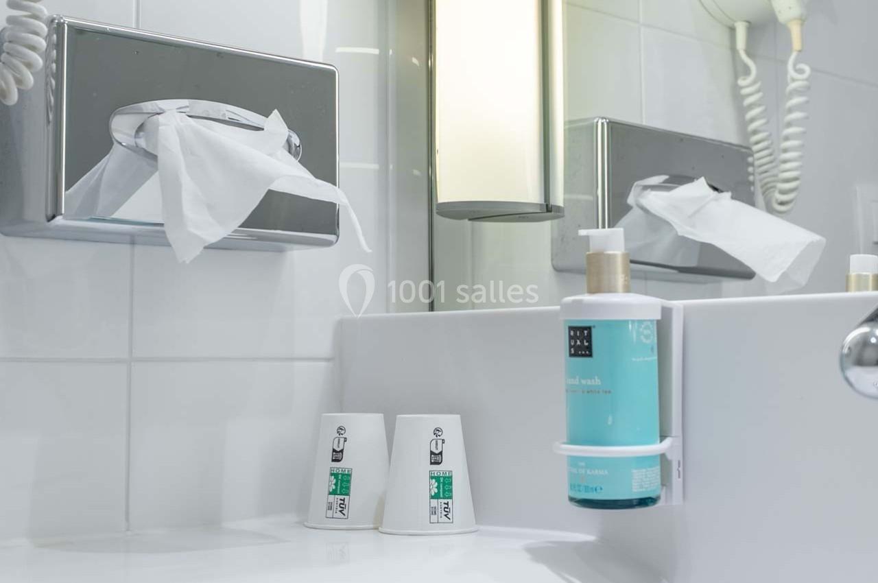 Distributeurs de mouchoirs et de savon liquide près d'un lavabo avec deux gobelets en plastique dans une salle de bain.