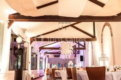 Groupe de personnes réunies en extérieur sous une structure métallique, devant un bâtiment en pierre et bois.