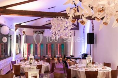 Groupe de personnes réunies en extérieur sous une structure métallique, devant un bâtiment en pierre et bois.