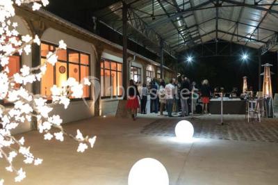 Groupe de personnes réunies en extérieur sous une structure métallique, devant un bâtiment en pierre et bois.