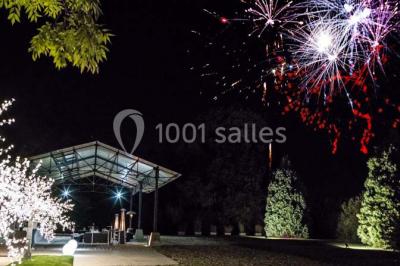 Groupe de personnes réunies en extérieur sous une structure métallique, devant un bâtiment en pierre et bois.