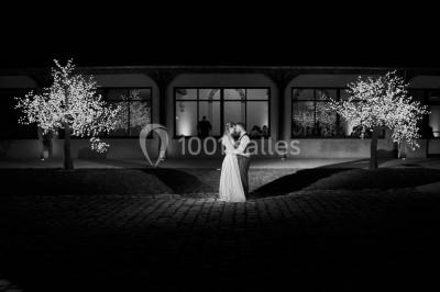 Groupe de personnes réunies en extérieur sous une structure métallique, devant un bâtiment en pierre et bois.
