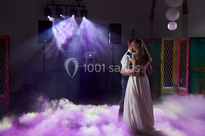 Groupe de personnes réunies en extérieur sous une structure métallique, devant un bâtiment en pierre et bois.