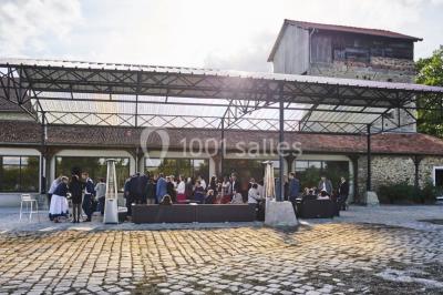 Groupe de personnes réunies en extérieur sous une structure métallique, devant un bâtiment en pierre et bois.