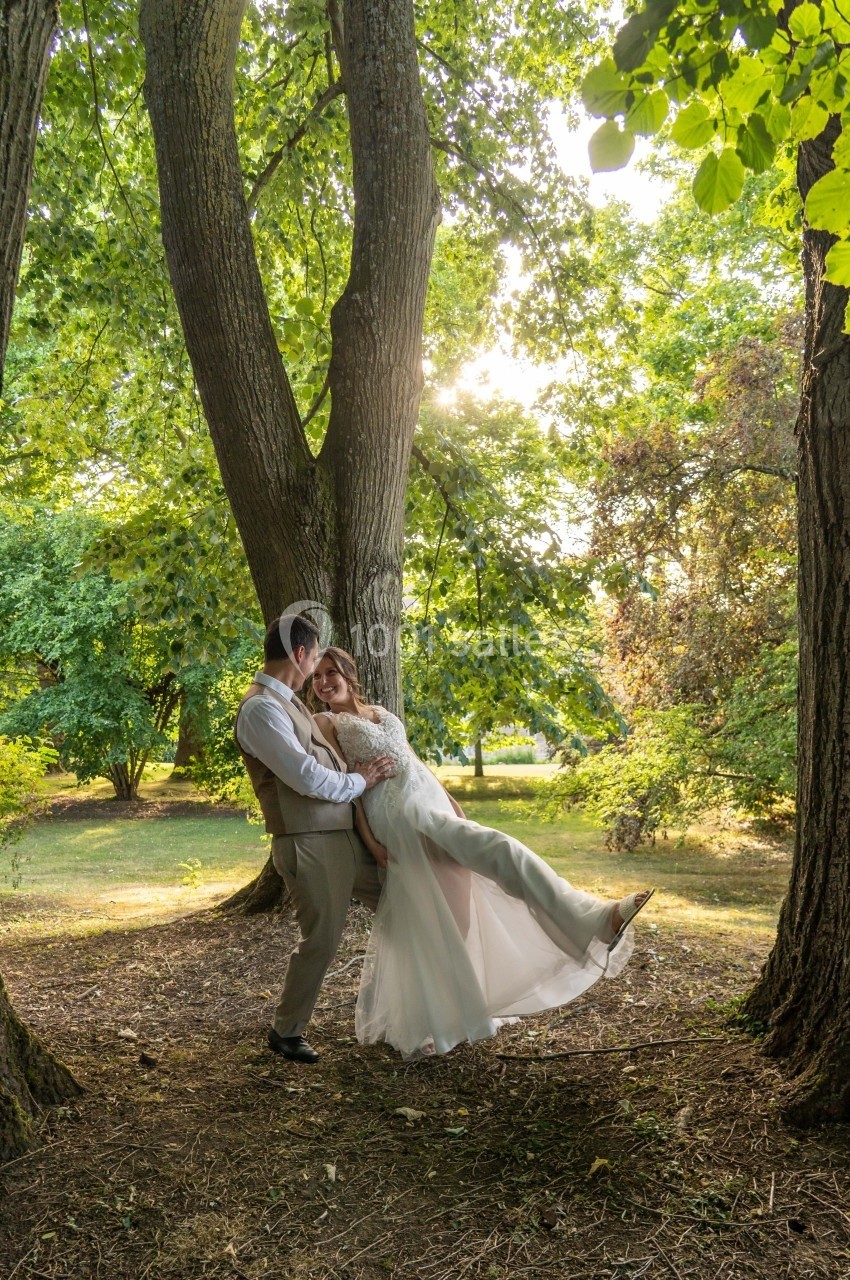 Un couple en tenue de mariage pose dans une clairière boisée baignée de lumière naturelle.