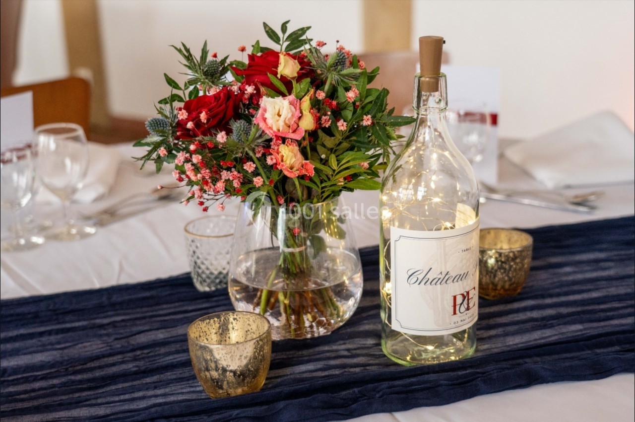 Bouquet de fleurs colorées et bouteille décorative illuminée posés sur une table avec nappe blanche et chemin bleu.