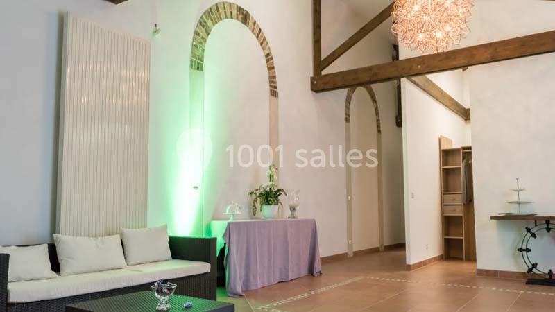 Salon lumineux avec canapé, table décorée, poutres apparentes, mur en arcs de briques et suspension design.