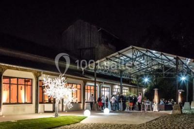 Bâtiment éclairé avec des fenêtres rouges, arbres décorés de lumières blanches et allée pavée de nuit.