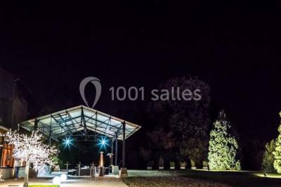 Bâtiment éclairé avec des fenêtres rouges, arbres décorés de lumières blanches et allée pavée de nuit.