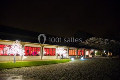 Bâtiment éclairé avec des fenêtres rouges, arbres décorés de lumières blanches et allée pavée de nuit.