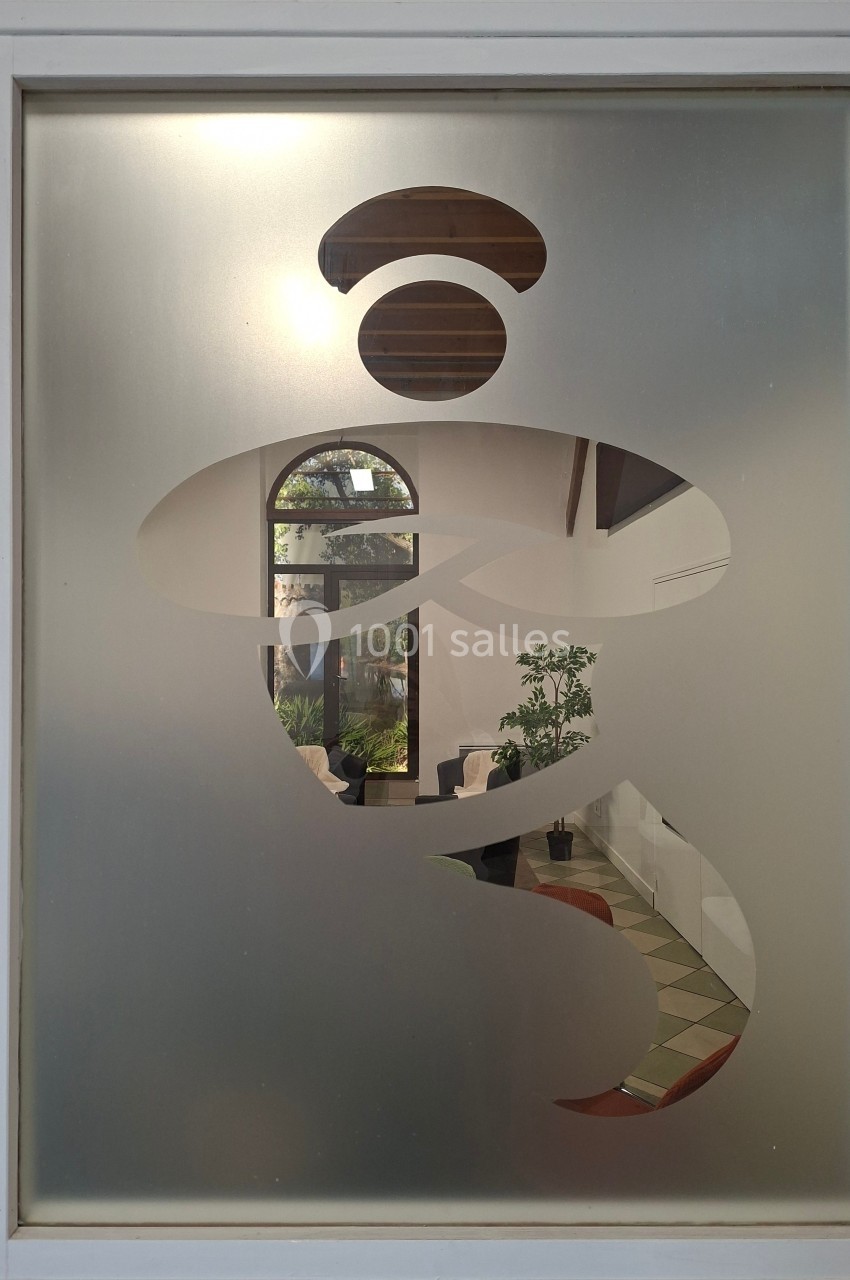 Découpe abstraite dans une vitre givrée laissant entrevoir un intérieur avec plantes et mobilier.