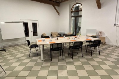 Salle de réunion avec une grande table rectangulaire, chaises noires, documents, bouteilles d'eau et écran de présentation.