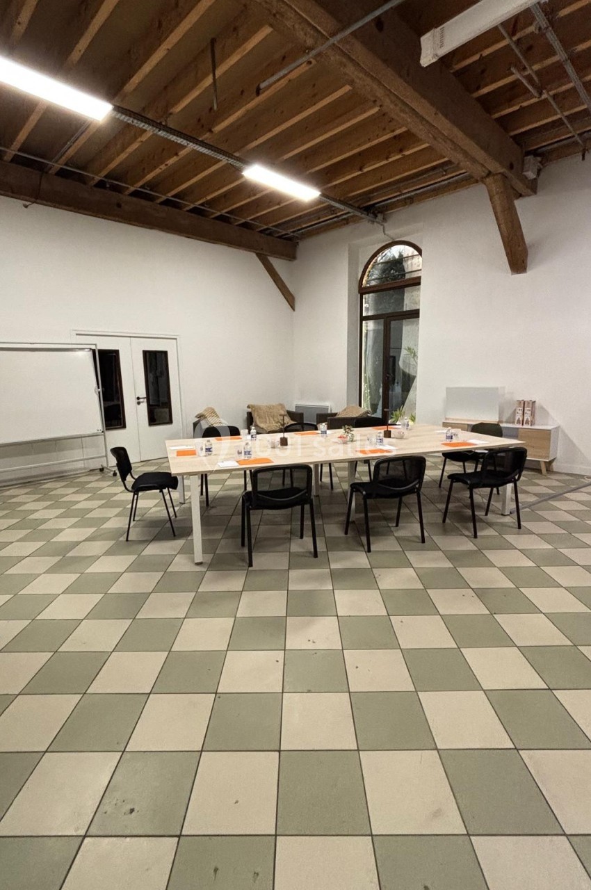 Salle de réunion avec une grande table blanche entourée de chaises noires, tableau blanc et canapé en arrière-plan.