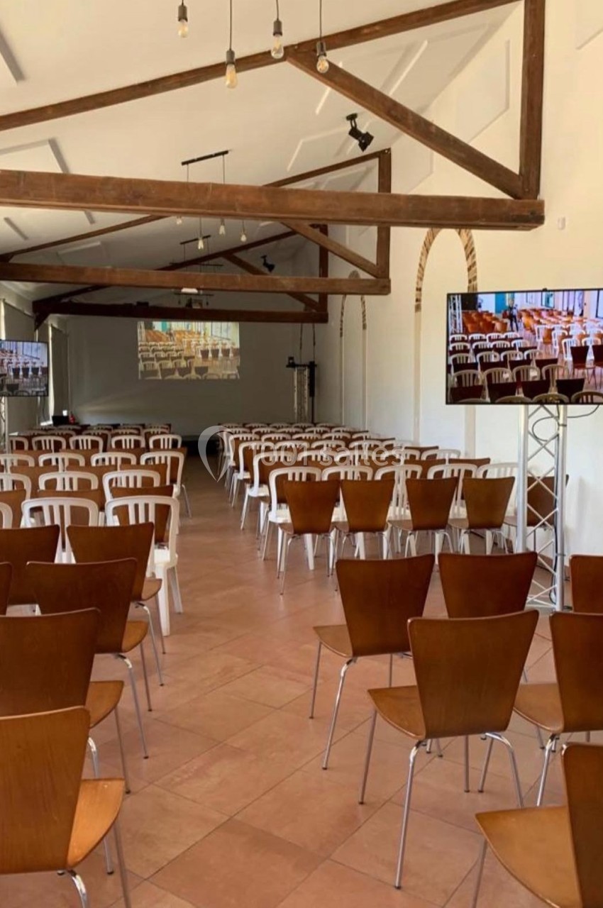 Salle de conférence lumineuse avec des rangées de chaises en bois et en plastique, écrans et poutres apparentes au plafond.