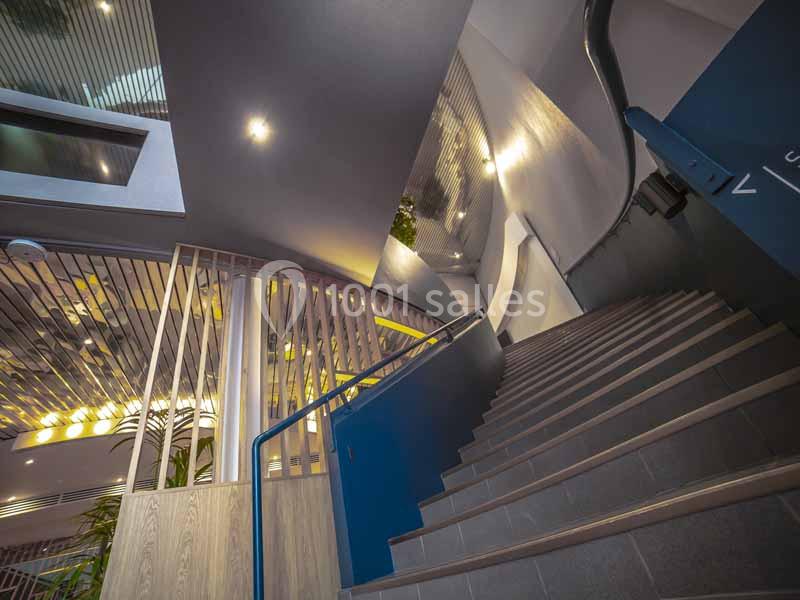 Escalier moderne en colimaçon avec rambarde bleue, éclairage intégré et éléments architecturaux contemporains.