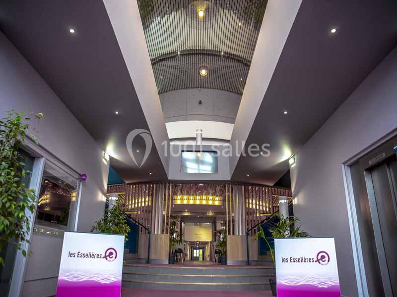 Vue intérieure d'un hall moderne avec un plafond voûté, des plantes et des panneaux indiquant ’les Esselières’.