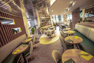 Miniature Brasserie Entrée d'un bâtiment avec escalier central, écrans d'affichage, plantes décoratives et sol en parquet.