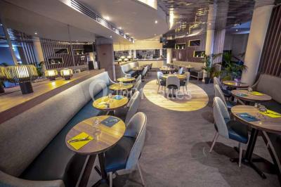 Miniature Brasserie Entrée d'un bâtiment avec escalier central, écrans d'affichage, plantes décoratives et sol en parquet.