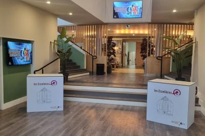 Miniature HALL D'ACCUEIL Entrée d'un bâtiment avec escalier central, écrans d'affichage, plantes décoratives et sol en parquet.