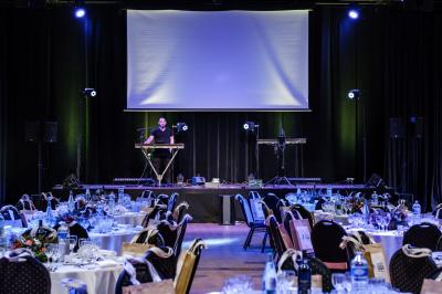 Miniature Salle Capella Entrée d'un bâtiment avec escalier central, écrans d'affichage, plantes décoratives et sol en parquet.