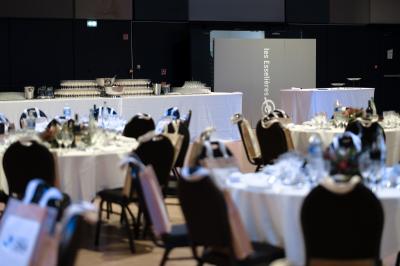 Miniature Salle Capella Entrée d'un bâtiment avec escalier central, écrans d'affichage, plantes décoratives et sol en parquet.