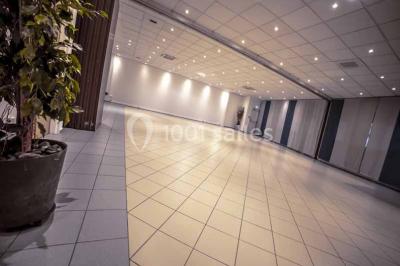 Miniature Salles du RDC modulables Entrée d'un bâtiment avec escalier central, écrans d'affichage, plantes décoratives et sol en parquet.