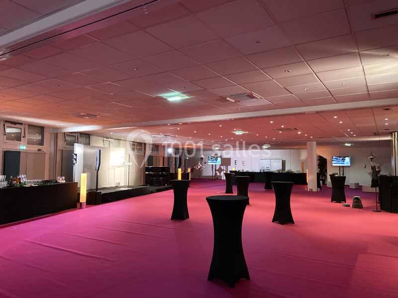 Salle de réception avec sol rose, tables hautes noires et éclairage tamisé, prête pour un événement.