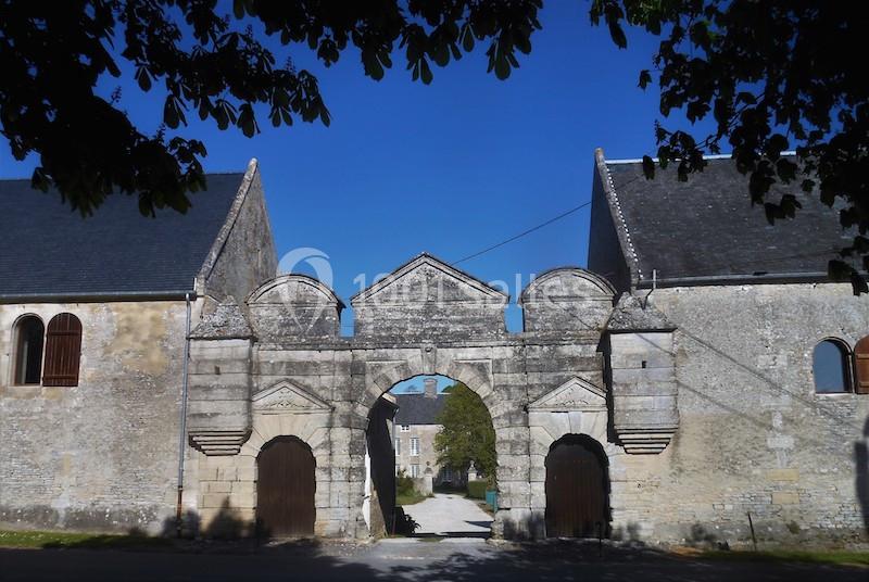 Portail en pierre d'une ancienne bâtisse avec deux ailes symétriques, sous un ciel bleu dégagé.