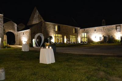 Vue nocturne d'une porte monumentale en pierre éclairée, avec un bâtiment blanc visible en arrière-plan.