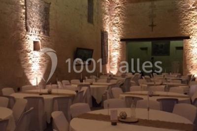 Vue nocturne d'une porte monumentale en pierre éclairée, avec un bâtiment blanc visible en arrière-plan.