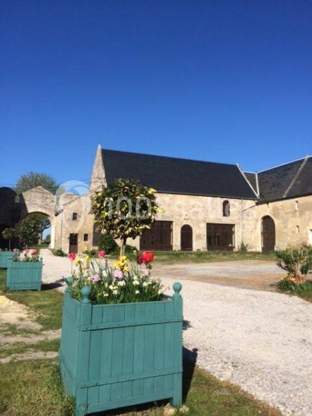 Bâtiments en pierre avec toits en ardoise, entourés de jardinières fleuries et d'une allée gravillonnée sous un ciel bleu.