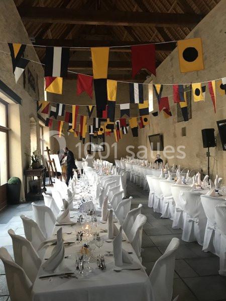 Salle de réception décorée de fanions colorés, avec de longues tables dressées et nappes blanches.