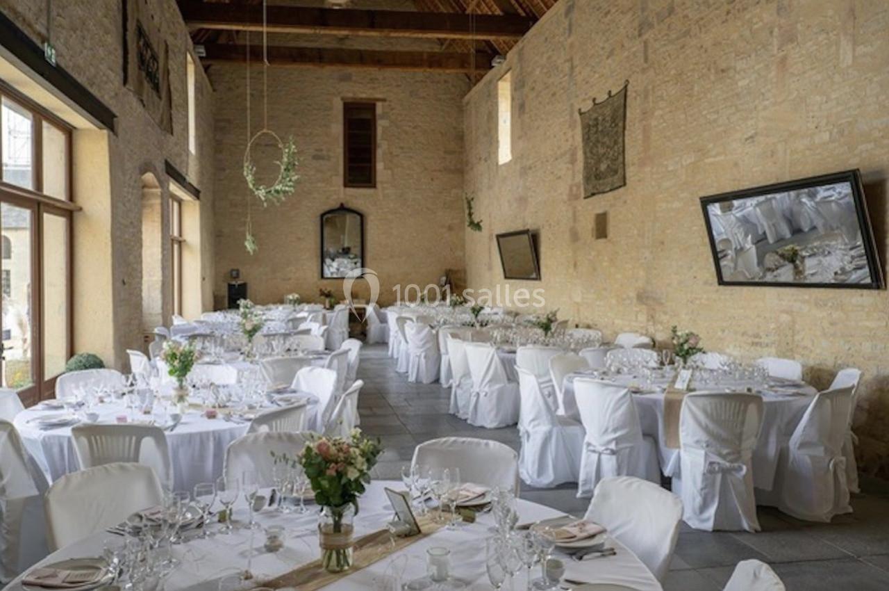 Salle de réception lumineuse avec tables rondes décorées de nappes blanches et compositions florales.