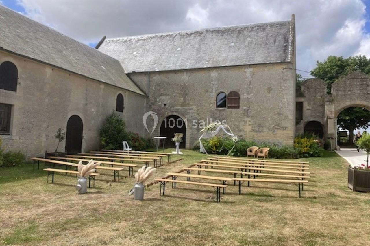 Bancs en bois disposés en extérieur devant un bâtiment en pierre, avec arche décorative et ciel partiellement nuageux.