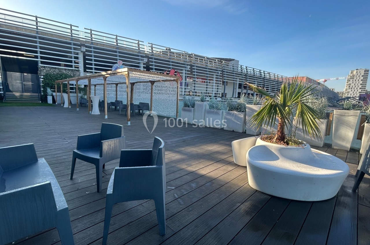 Terrasse en bois avec mobilier extérieur, pergola, plantes en pots et vue sur des bâtiments modernes.