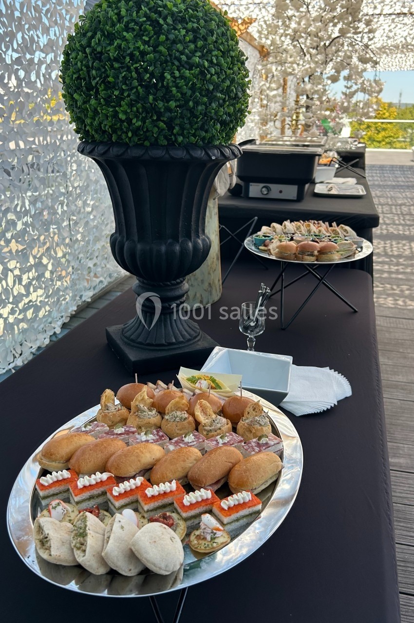 Plateaux de canapés variés disposés sur une table noire, avec une décoration végétale en arrière-plan.