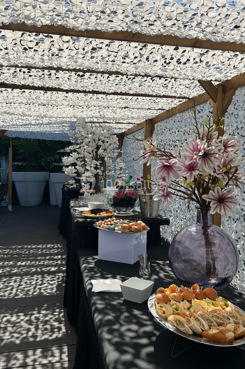 Buffet en extérieur sous une pergola ombragée, avec des plats variés et des décorations florales.