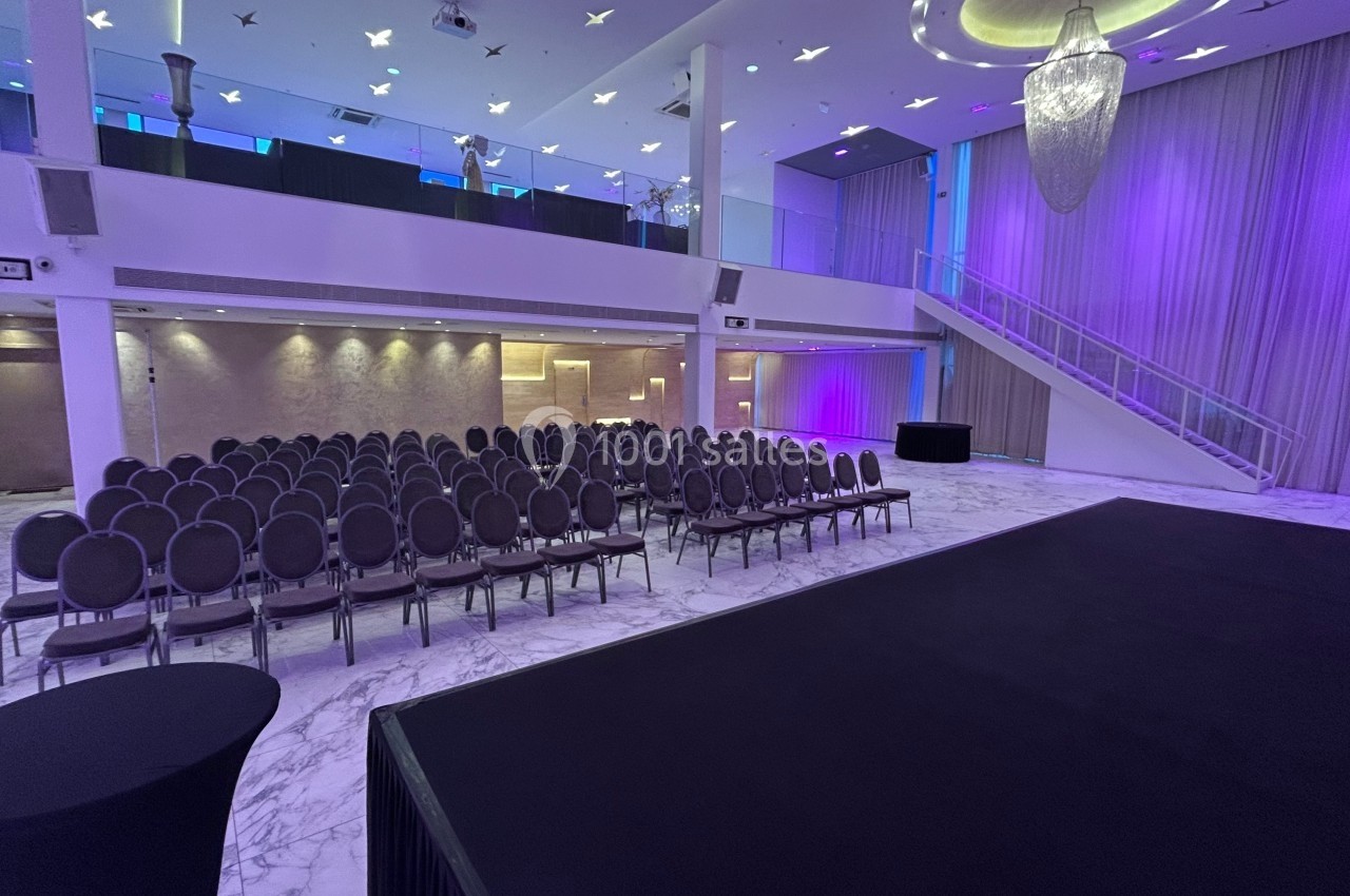 Salle de conférence moderne avec scène, rangées de chaises alignées et éclairage violet.