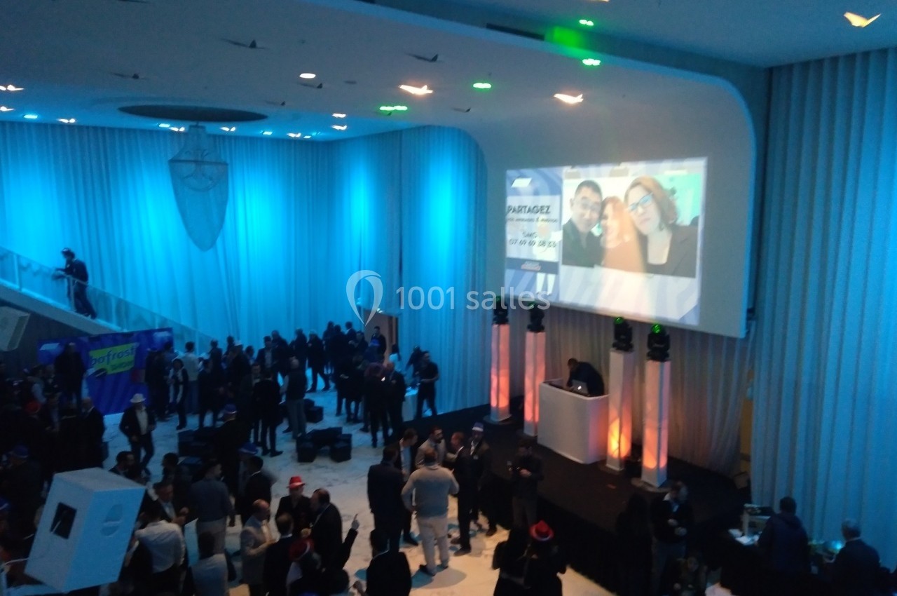 Salle de réception avec des invités rassemblés, éclairage bleu et projection d'images sur un mur.