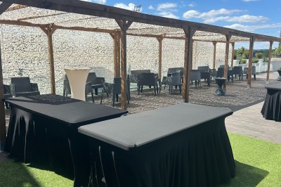 Miniature Location salle Villeurbanne (Rhône) - Le Pavillon De La Soie #18 Terrasse avec pergola en bois, tables et chaises noires, sol en bois et gazon artificiel, ciel bleu en arrière-plan.