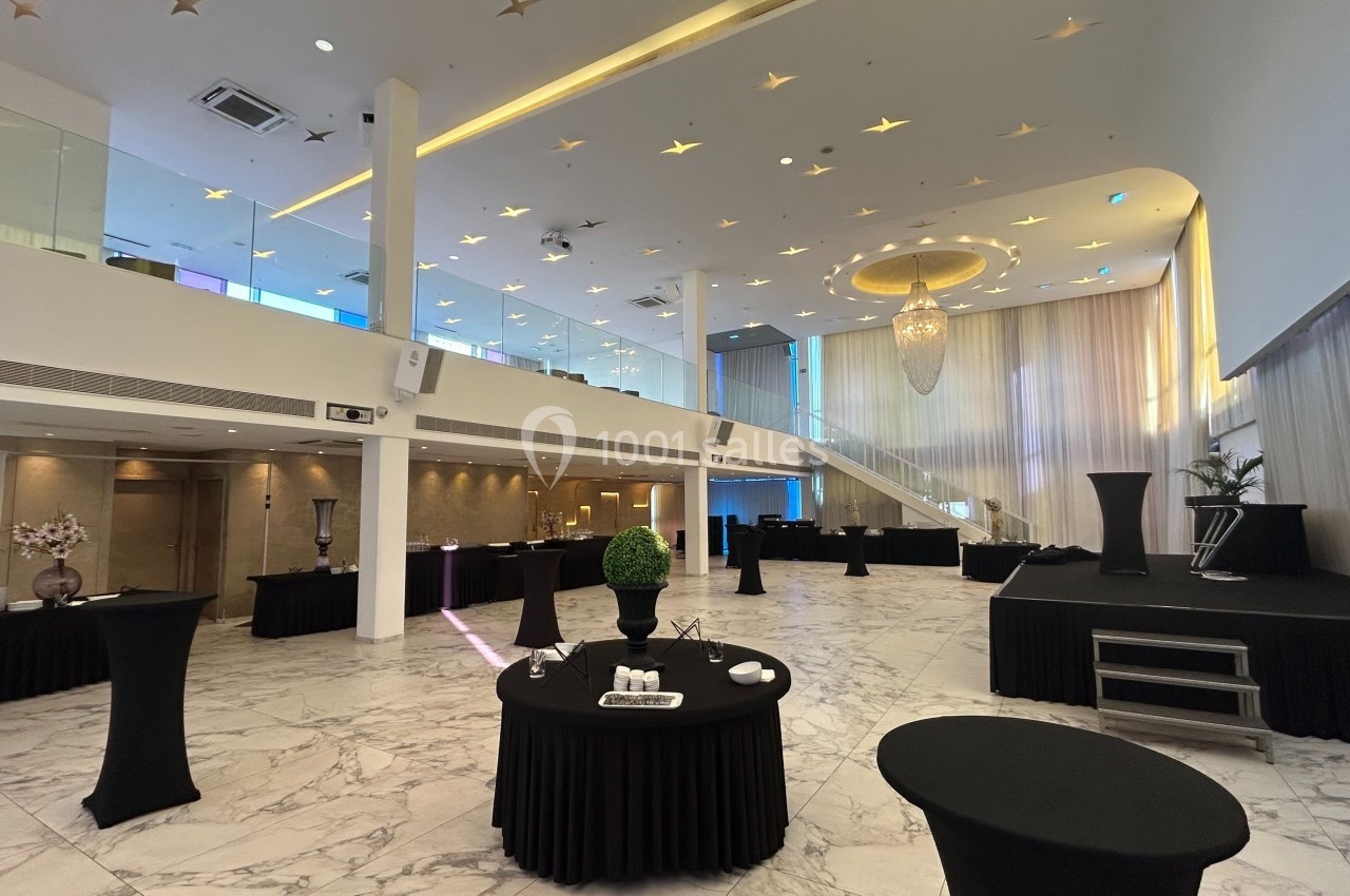 Salle de réception spacieuse avec mezzanine, tables hautes noires et éclairage chaleureux sous un plafond étoilé.