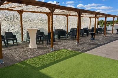 Miniature Location salle Villeurbanne (Rhône) - Le Pavillon De La Soie #38 Terrasse avec pergola en bois, tables et chaises noires, sol en bois et gazon artificiel, ciel bleu en arrière-plan.