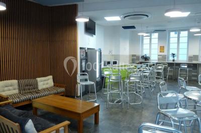 Terrasse extérieure avec des tables rondes et des chaises rouges et noires, entourée de végétation et de barrières…