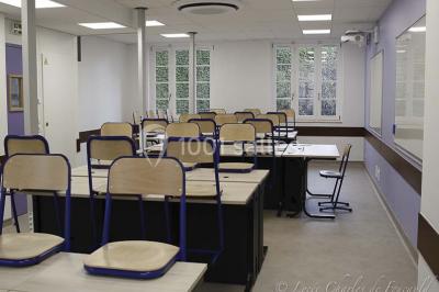 Terrasse extérieure avec des tables rondes et des chaises rouges et noires, entourée de végétation et de barrières…