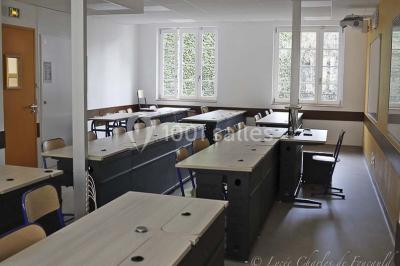 Terrasse extérieure avec des tables rondes et des chaises rouges et noires, entourée de végétation et de barrières…