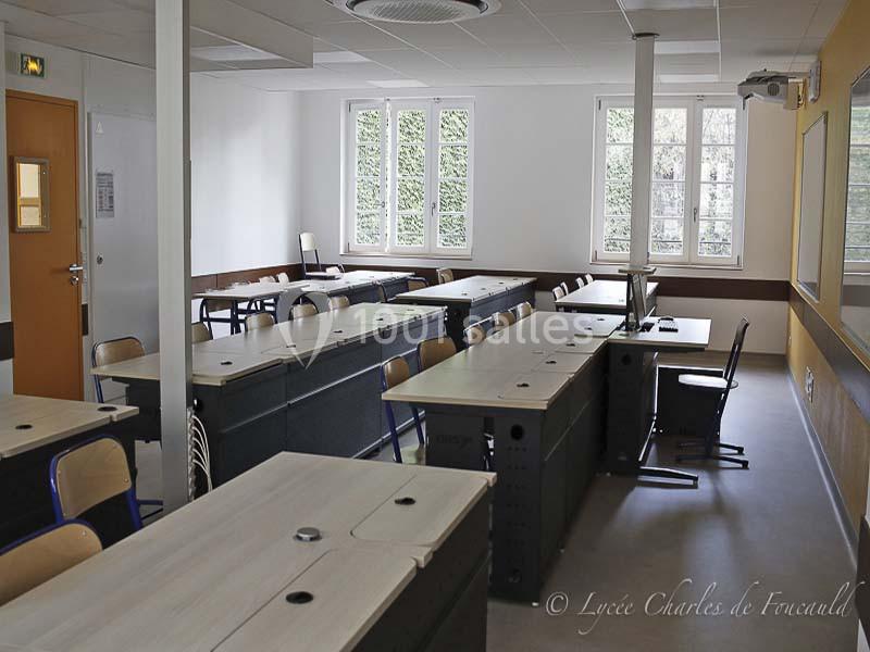 Salle de classe vide avec des bureaux alignés, des chaises en bois, un tableau blanc et des fenêtres donnant sur un espace…